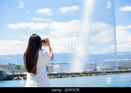 Asian beautiful woman is travel for holiday in the summer of Europe and taking a camera view landscape of lake and bright sky in Geneva Switzerland, c