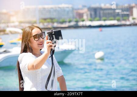 Asian beautiful woman is travel for holiday in the summer of Europe and taking a camera view landscape of lake and bright sky in Geneva Switzerland, c