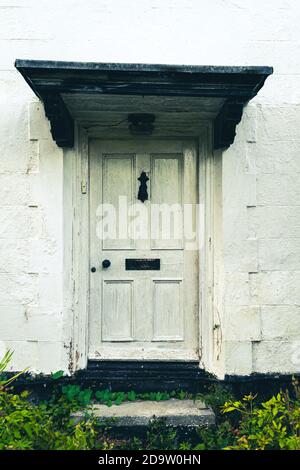 Beautiful rural white rustic door with overgrown by weeds stairs, british countryside house in the middle of nowhere. Stock Photo