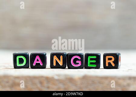 Black bead with color letter in word danger on wood background Stock Photo