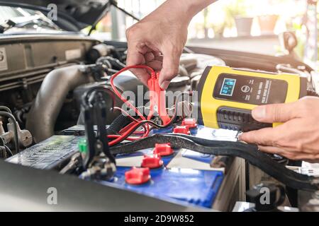 The car mechanic is using a voltage measuring instrument and charging the battery, the car's battery power. Stock Photo