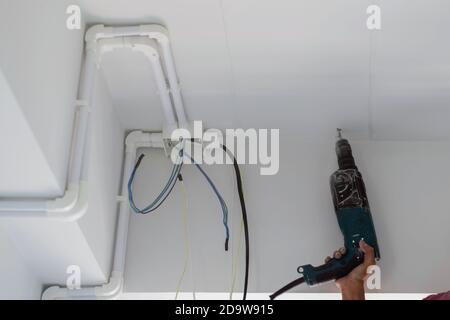 Technicians are using electric drills to penetrate the ceiling of the room for pipe clamps for electrical wires inside the building. Stock Photo