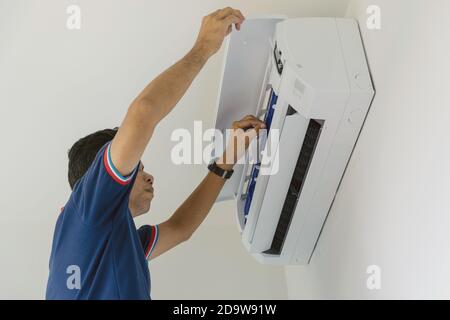 Air conditioner repairers in blue uniform are checking and repair air hanging on the wall. Stock Photo