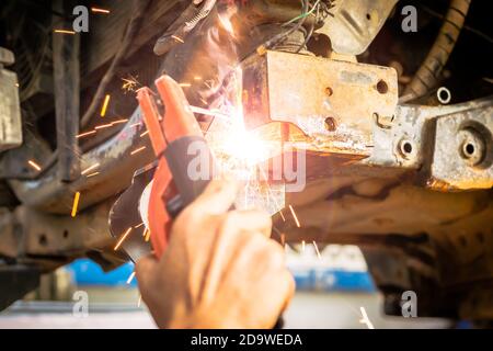 Technician are welding assembly steel under the car in automotive industrial factory -Automotive industry and garage concepts. Stock Photo