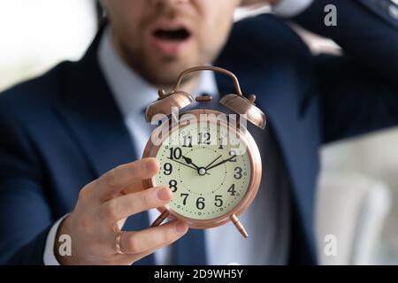 Worried young male manager employee in formal wear holding clock. Stock Photo