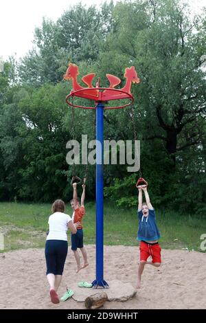 Children on rotating rope swing around central pole in park Stock Photo
