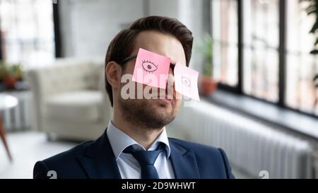 Exhausted businessman sitting in office with paper stickers on eyeglasses. Stock Photo