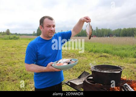 Man puts fish into cauldron for cooking russian fish soup - ukha Stock Photo