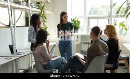 Confident young lady trainer gives recommendations to diverse employee group Stock Photo