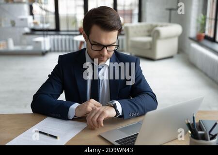Focused serious young businessman in suit checking time on wristwatch. Stock Photo