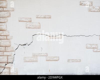 A wall with decorative plaster in the form of masonry with a large crack. Background texture. Full-screen Stock Photo