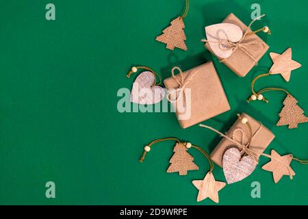 Christmas gifts wrapped in craft paper on a green background. Christmas gifts and Christmas wooden decorations with place for text. Copy space. Yop view. Flat lay Stock Photo