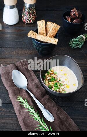 Freshly cooked chestnut soup in a brown ceramic bowl, decorated with chestnut pieces and parsley on a brown wooden table with salt and pepper shakers, Stock Photo