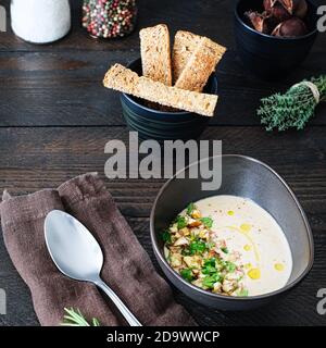 Freshly cooked chestnut soup in a brown ceramic bowl, decorated with chestnut pieces and parsley on a brown wooden table with salt and pepper shakers, Stock Photo