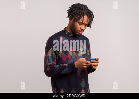 Profile portrait concentrated serious african man holding mobile phone in hands reading message, checking email, chatting in social networks. Indoor s Stock Photo