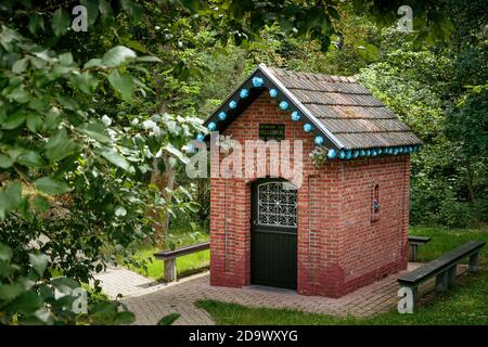 Kortenaken, Flanders, Belgium - July 9 2017 : small brick chapel 'Onze-Lieve-Vrouw van de Dellebron' decorated with blue paper flowers, surrounded by Stock Photo