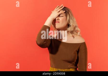Facepalm. Portrait of unhappy young woman with blonde hair in casual clothes standing with hand on head,feeling sorrow regret blaming herself for fail Stock Photo