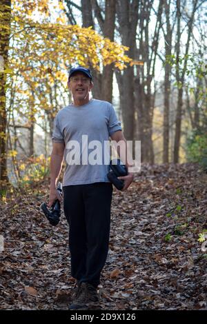 Caucasian man hiking in the Autumn woods carrying a tripod Stock Photo