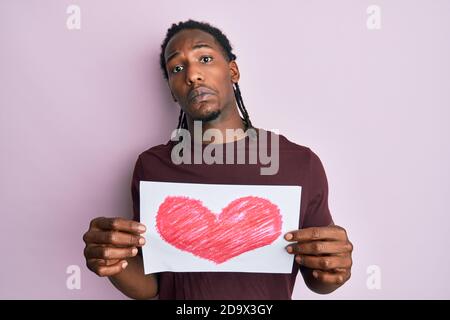 African american man with braids holding heart draw clueless and confused expression. doubt concept. Stock Photo