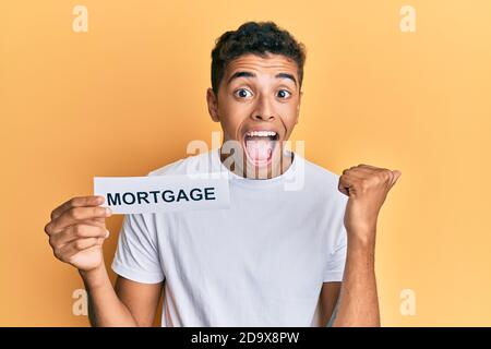 Young handsome african american man holding mortgage word pointing thumb up to the side smiling happy with open mouth Stock Photo