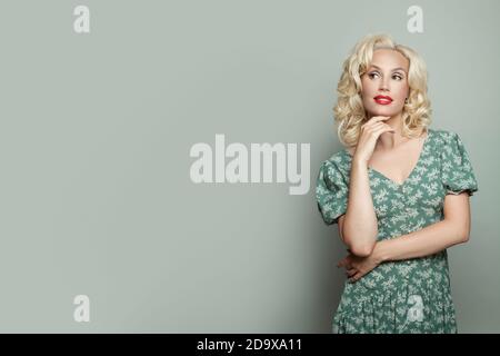 Attractive woman with makeup and blonde curly hair wearing green dress on light  green banner background Stock Photo - Alamy