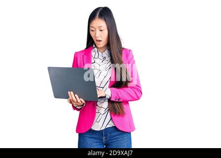 Young beautiful chinese woman using laptop scared and amazed with open mouth for surprise, disbelief face Stock Photo
