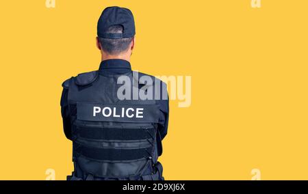 Young hispanic man wearing police uniform standing backwards looking away with crossed arms Stock Photo