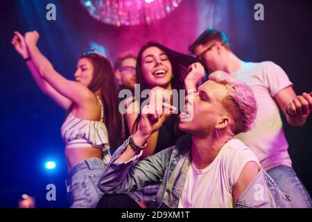 Guy taking drug pill. Young people is having fun in night club with colorful laser lights Stock Photo
