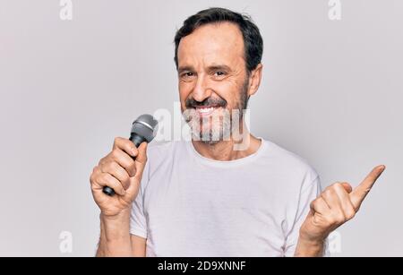 Middle age handsome singer man singing using microphone over isolated white background smiling happy pointing with hand and finger to the side Stock Photo