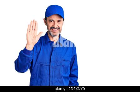 Middle age handsome man wearing mechanic uniform waiving saying hello happy and smiling, friendly welcome gesture Stock Photo