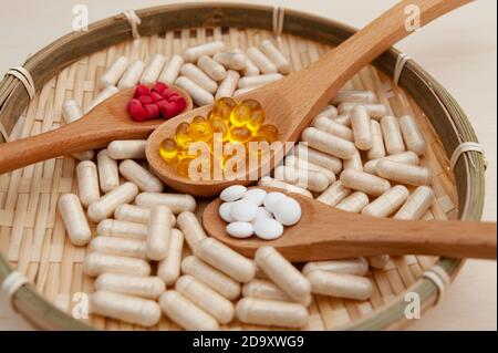 Healthy lifestyle - Vitamins, minerals and nutritional supplements in wooden spoons inside a braided bamboo plate. Close-up. Stock Photo