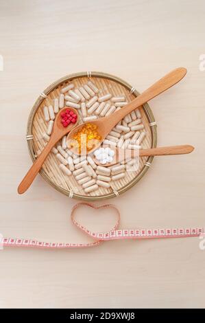 Healthy lifestyle - Vitamins, minerals and nutritional supplements in wooden spoons inside a braided bamboo plate with a heart shaped soft vinyl tape. Stock Photo