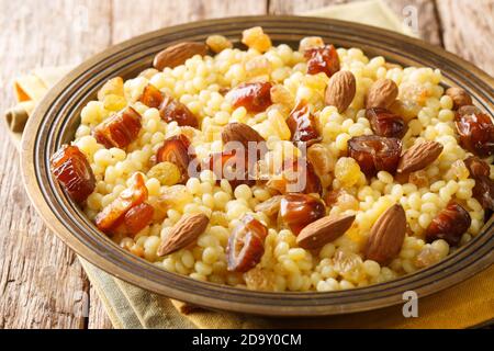 Sweet couscous with almonds, raisins and dates close-up in a plate on the table. Horizontal Stock Photo