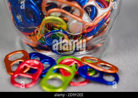 a close up view of the bottom of the jar of multi colored can pull tabs and some lying loose Stock Photo