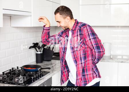 Young man seasoning food at home kitchen in apron baking cookies, adding flaworings to dough and having fun Stock Photo