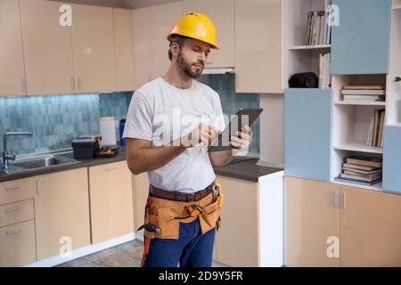 Builder in helmet working with tablet on kitchen background Stock Photo