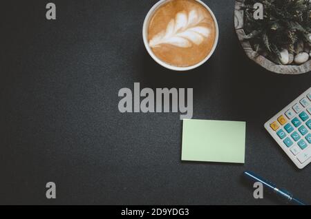Top view office desk with calculator, coffee mug, pen and cactus on vintage tone black background..Flat lay copy space. Stock Photo