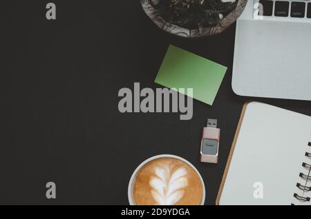 Office desk with notepad, coffee, leaf and computer laptop on black background.Top view copy space. Stock Photo