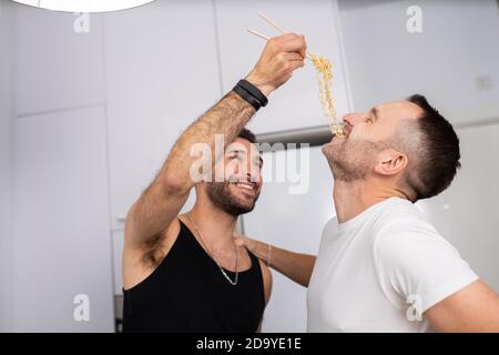 Man feeding pasta to his boyfriend in a fun way Stock Photo