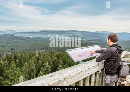 Man on observation tower looking in a map.Male backpacker enjoying view of misty landscape.Man Traveler on Czech Boubin mountain summit.Travel Stock Photo