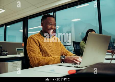 Multi-ethnic male designer working on business report typing on laptop next to female entrepreneur in office Stock Photo