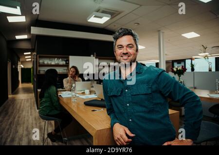 Portrait of smiling caucasian business man sitting against office table enjoying lunch break  Stock Photo