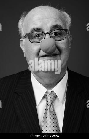 Overweight senior businessman wearing clown's nose against brown background Stock Photo