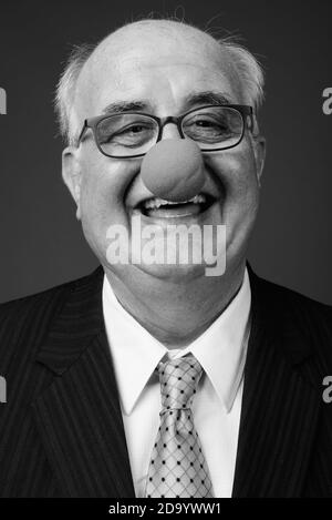 Overweight senior businessman wearing clown's nose against brown background Stock Photo