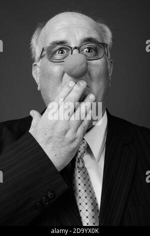 Overweight senior businessman wearing clown's nose against brown background Stock Photo