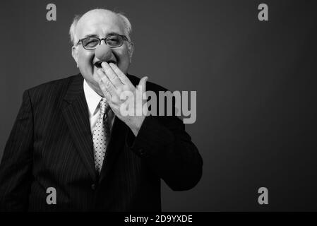 Overweight senior businessman wearing clown's nose against brown background Stock Photo