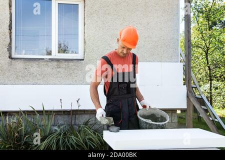 Insulation of the house with polyfoam. The worker is applying adhesive to the polystyrene board. Stock Photo
