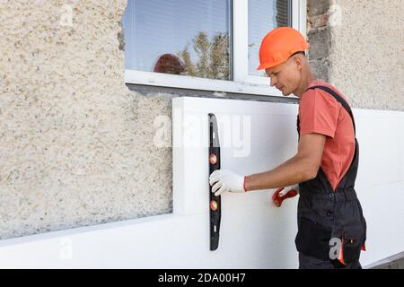 Insulation of the house with polyfoam. The worker is checking with the construction level the accuracy of the installation of polystyrene board on the Stock Photo