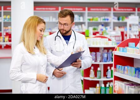 team of young caucasian chemists or druggists discussing medicines, check medical indications, in white medical gowns, at work place Stock Photo