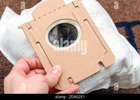 close-up of vacuum cleaner bag in hand, filled dust and animal hair on brown mat background Stock Photo